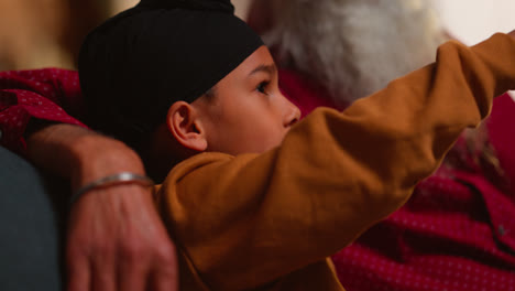 Smiling-Sikh-Grandfather-And-Grandson-Wearing-Turbans-Sitting-On-Sofa-At-Home-Talking-Together-Shot-In-Real-Time